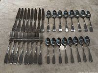 Full set of 24 stainless steel cutlery pieces arranged in rows with knives, forks, and spoons shown on marble surface.
