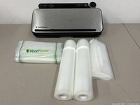 Full view of FoodSaver vacuum sealer unit along with vacuum seal rolls and FoodSaver branded bags on table surface.