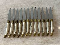 Top view of 12 Laguiole steak knives laid in a row on marble surface