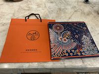 Photo of orange Hermes paper bag and decorative scarf box on a marble surface.