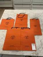Set of 5 Hermes orange paper shopping bags arranged on table showing varying sizes and logo