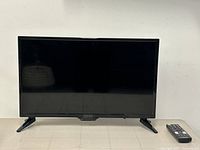 Frontal view of the black Insignia 24-inch flat screen TV showing the screen, stand, and remote control on the right side.
