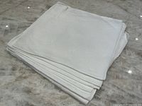 Stack of seven folded white dinner napkins on a marble surface.