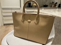 Front view of the tan leather tote bag showing two handles and oval stitched detail.