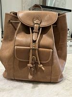 Front view of tan leather knapsack showing front flap with buckle and pocket.