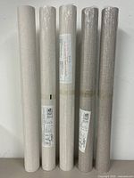 Five wallpaper rolls standing upright, beige and taupe shades visible in plastic wrapping, showing unopened condition except one.