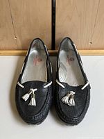 Top front perspective showing the pair of black textured leather golf moccasins with white tassels and lace detail.