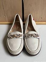Angled front view showing white leather moccasin toes and braided gold-tone hardware, highlighting overall shoe condition and shape.