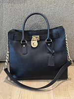 Front view of black leather handbag showing gold lock and chain strap detail.