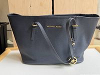 Front view of navy blue Michael Kors leather tote bag with gold logo and MK charm visible on strap.