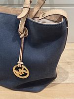 Close-up of canvas exterior navy blue tote with tan leather handle and gold-tone MK logo charm