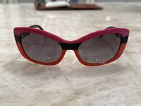 Front view of Prada women's sunglasses with bright pink and orange frame and dark lenses showing color details and shape