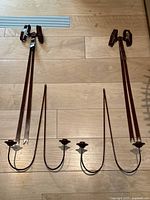 Full view of the pair of red painted metal sconces laid on wooden floor, showing ribbon bow design and two candle holders each.