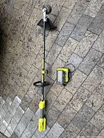Full view of string trimmer attachment, battery pack and charger on stone patio