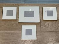 Four gold metal picture frames laid out on a wood surface, showing two smaller square frames, one larger rectangular frame, and one additional smaller square frame.
