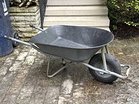 Left side view of black steel wheelbarrow with tubular steel handles and frame, showing overall structure and condition.