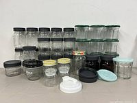 Various sized clear glass storage jars with lids arranged in rows, black lids on majority, some green, yellow plaid, and light blue lids.