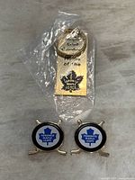 Photo of the gold-colored metal keychain in packaging and two hockey pins with the Toronto Maple Leafs logo.