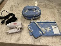 Compact white travel hairdryer with red BaByliss logo, small white clothing iron, and set of three quilted blue floral makeup bags displayed on marble surface.