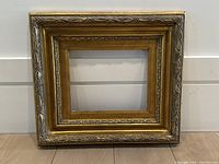 Front view of vintage ornate gilt wooden picture frame with intricate carved detailing and minor wear visible on edges and corners.