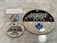 Top-down photo showing the three buttons laid flat: large team photo button, smaller team photo button with text, and Harold Ballard button.