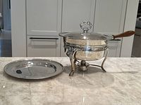 Full view of W.M. Rogers silver plated round chafing dish with burner and separate round serving tray placed on countertop