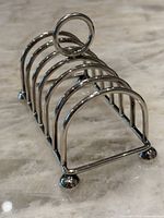 Side angle view showcasing the five semi-circular arches, feet, and handle of the silver plated toast rack.