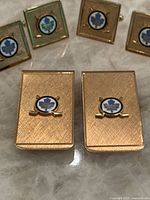 Close-up of gold-tone rectangular cufflinks with textured background and Toronto Maple Leafs logo in blue and white enamel centered above crossed hockey sticks.