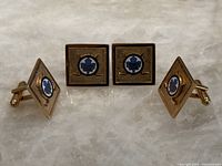 Two pairs of gold-toned metal Toronto Maple Leafs cufflinks. Front enamel logos with crossed hockey sticks on textured square and diamond shapes.