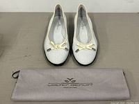 Pair of Walter Genuin white perforated leather golf shoes with soft yellow patent bows and silver hardware, placed on a gray cloth bag bearing Walter Genuin logo.