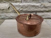 Front angle view of hammer-textured copper saucepan with lid and long brass handle