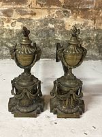 Front view of the pair of antique bronze fireplace andirons showing urn-topped andirons with flame finials and rams head detail