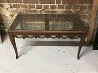 Full view of rectangular antique walnut coffee table with glass top, placed against brick wall, showing overall shape and condition.