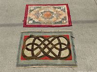Two antique hooked rugs placed on pavement, one with a floral diamond medallion design and the other with an interlaced ribbon pattern.