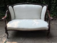 Front view of antique loveseat showing carved wood frame and white upholstery.