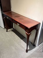 Side angle view of the antique style wooden console table showing the two drawers and cabriole legs with wear on the top surface.