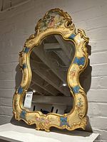 Entire wall mirror showing frame with floral details and blue accents on cream base. Mirror glass reflecting background conditions.