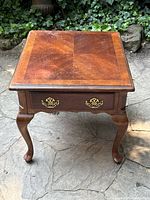Front view of mahogany side table showing the wood top with sunburst grain pattern, single drawer with brass handles, and cabriole legs.