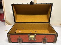 Open orange antique style storage trunk showing yellowish textured interior lining, brass latch and corner reinforcements.