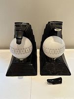 Front view of both black ceramic wave lamps with white patterned globe shades; shows broken off wave tip piece on table