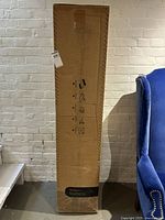 Full view of boxed mattress leaning against wall next to blue chair