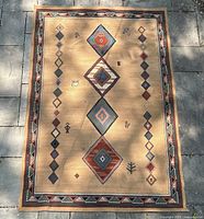 Top view of rectangular beige rug with central geometric diamond patterns and multi-colored border.