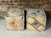 Pair of vintage style pastel patchwork ottomans side by side on concrete floor with brick wall background.
