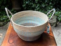 Front and side view of the woven basket showing turquoise stripes and looped handles, new with tag attached.