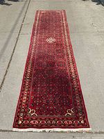 Full-length view of red Persian runner rug laid out on pavement showing overall pattern and condition.