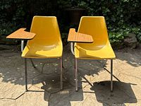 Front view of two yellow fibreglass classroom chairs with attached woodgrain desks and chrome legs set outdoors, showing the overall design and color.
