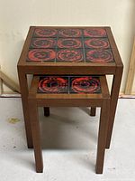 Stacked view of three solid teak nesting tables with red and black abstract tiled tops.