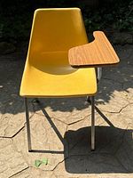 Front-left angled view showing yellow fiberglass seat, chrome legs, and wood veneer writing tablet.