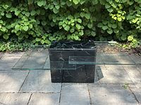 View of the coffee table from the side showing the clear glass top tier and black faux marble base tier with geometric block shape.