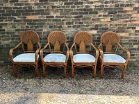 Front view of the set of four vintage boho rattan chairs with some cushions in light blue and others patterned upholstery, arranged against a brick wall.